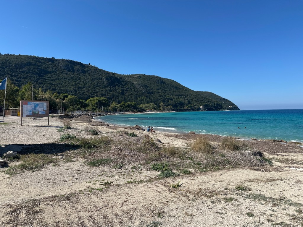 A scenic view of a beach on Lefkada with mountains in the background and a clear blue sky.